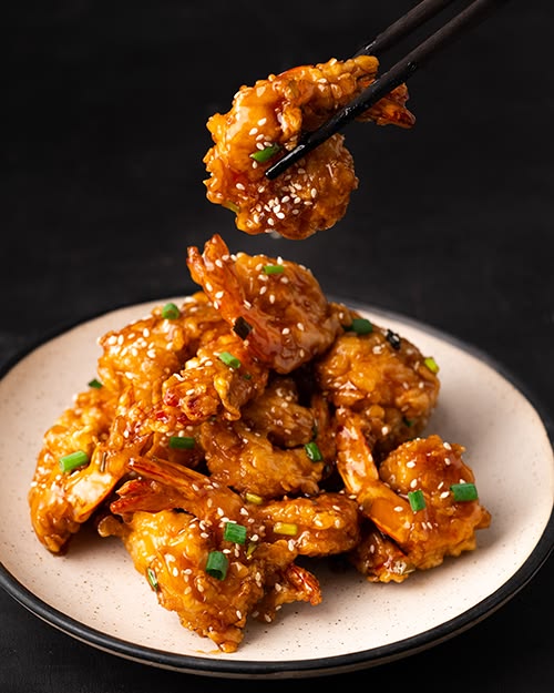 Golden sesame chilli prawns glazed and glossy, lifted with chopsticks